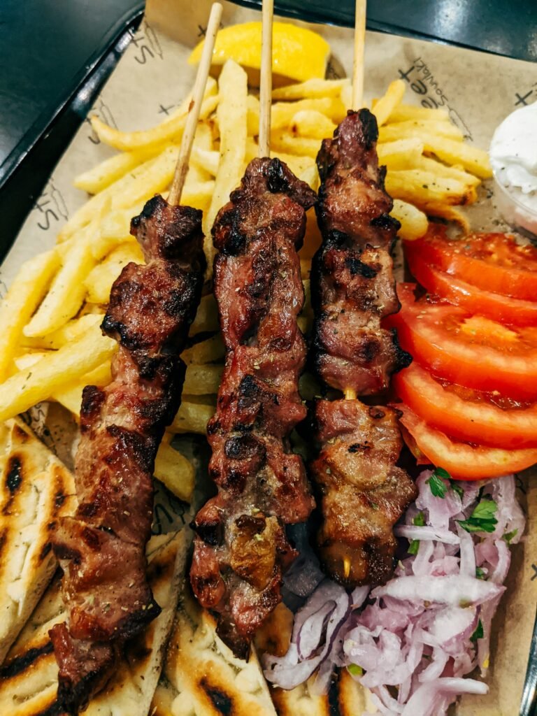 Grilled meat skewers with fries, sliced tomatoes, red onions and pita
